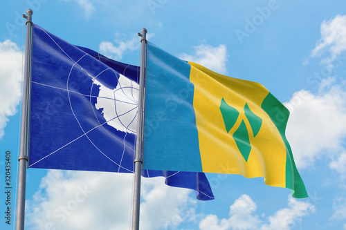 Saint Vincent And The Grenadines and Antarctica flags waving in the wind against white cloudy blue sky together. Diplomacy concept, international relations.