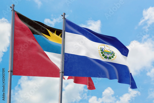 El Salvador and Antigua and Barbuda flags waving in the wind against white cloudy blue sky together. Diplomacy concept, international relations.