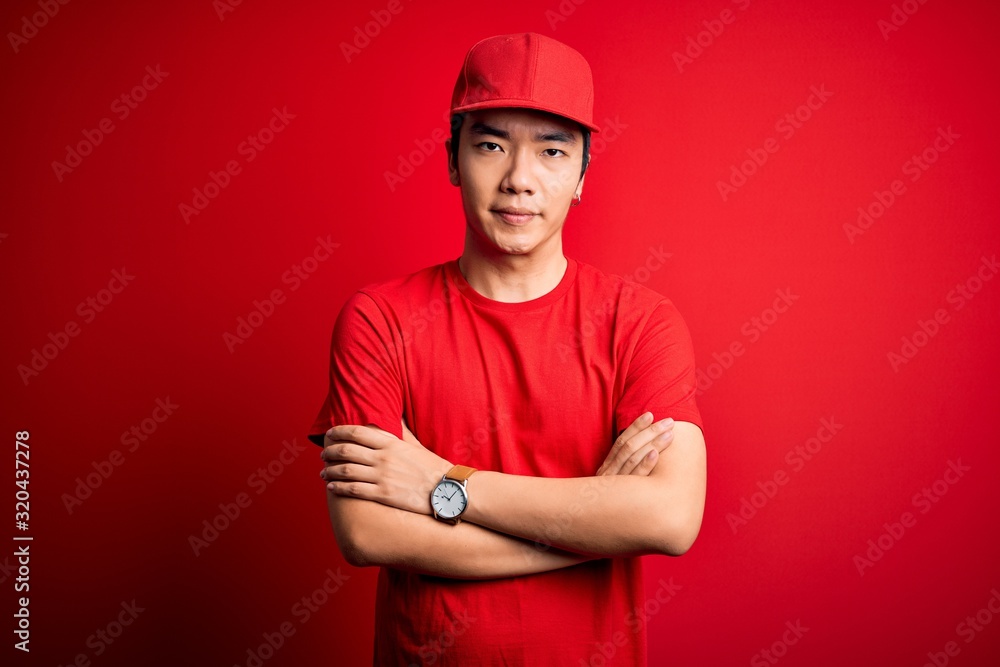 Young handsome chinese delivery man wearing cap standing over isolated red background skeptic and nervous, disapproving expression on face with crossed arms. Negative person. Young handsome chinese delivery man wearing cap standing over isolated red background skeptic and nervous, disapproving expression on face with crossed arms. Negative person.