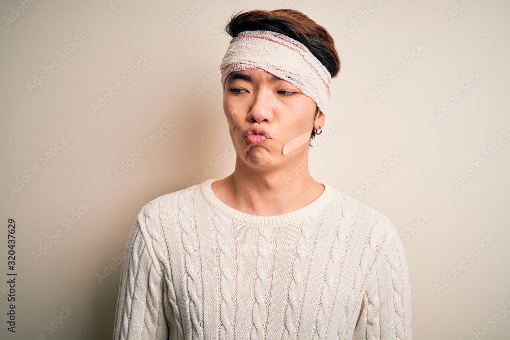 Young handsome chinese man injured for accident wearing bandage and strips on head making fish face with lips, crazy and comical gesture. Funny expression. Young handsome chinese man injured for accident wearing bandage and strips on head making fish face with lips, crazy and comical gesture. Funny expression.