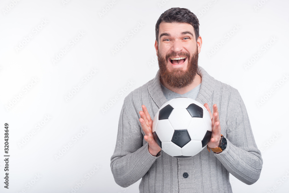 Sports betting. Bearded man is holding a soccer or football ball, having an excited face on white background. Sports betting. Bearded man is holding a soccer or football ball, having an excited face on white background.