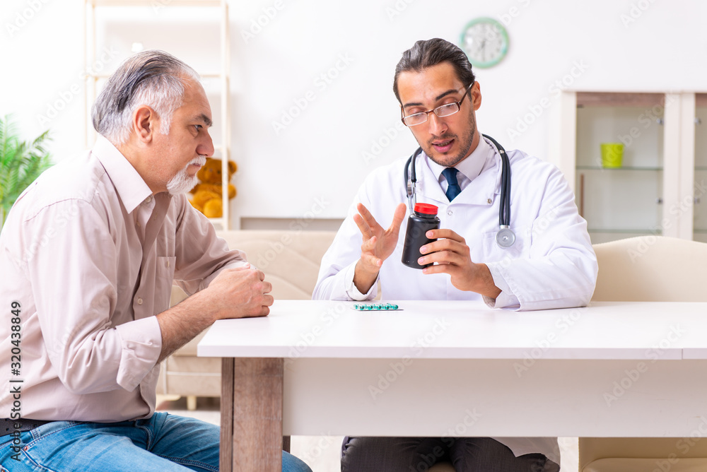Fototapeta premium Young male doctor visiting old patient at home