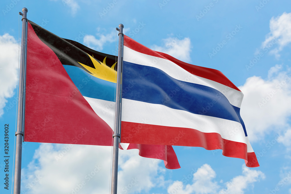 Thailand and Antigua and Barbuda flags waving in the wind against white cloudy blue sky together. Diplomacy concept, international relations.
