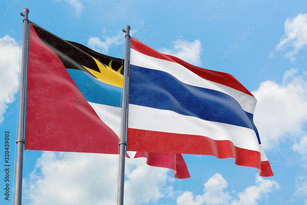 Thailand and Antigua and Barbuda flags waving in the wind against white cloudy blue sky together. Diplomacy concept, international relations. Thailand and Antigua and Barbuda flags waving in the wind against white cloudy blue sky together. Diplomacy concept, international relations.