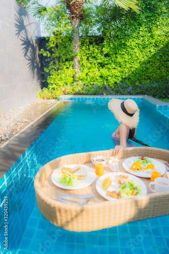 Portrait young asian woman happy smile enjoy with floating breakfast tray in swimming pool in hotel