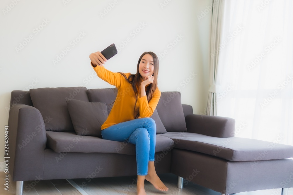 Portrait young asian woman using smart mobile phone on sofa with pillow in living room