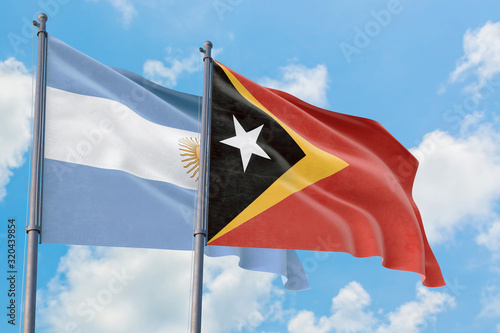 East Timor and Argentina flags waving in the wind against white cloudy blue sky together. Diplomacy concept, international relations.