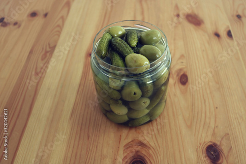 isolated glass jar with fresh green olives mixed with pickles on a wooden table - healthy mediterranean food