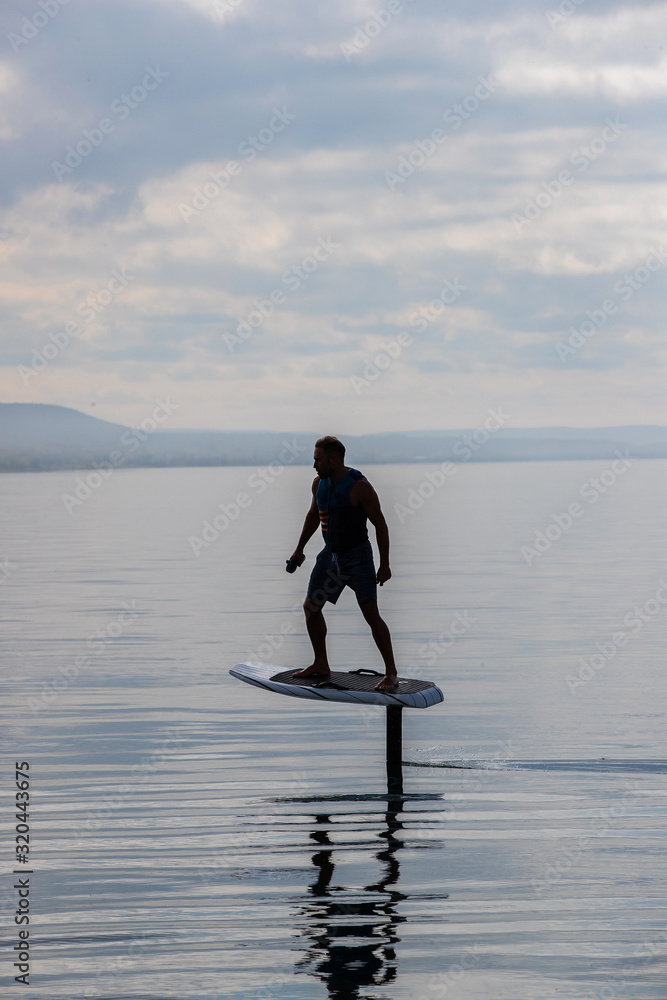 Man riding an electric hydrofoil foil board on a lake with a life jacket