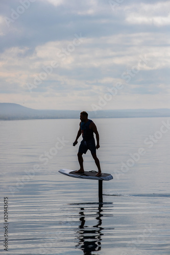 Obraz na płótnie Man riding an electric hydrofoil foil board on a lake with a life jacket w salonie