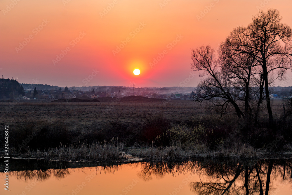 Flame-colored sunset over water, halo in the form of an arc