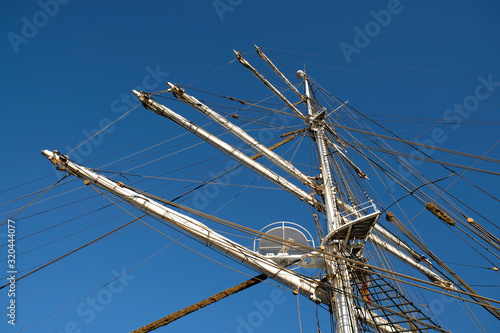 The main mast and yards of a romantic classic sailing ship, visible shrouds, stays, mast nest,  and complex rigging, blue sky in the background.