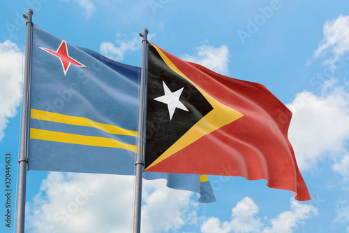 East Timor and Aruba flags waving in the wind against white cloudy blue sky together. Diplomacy concept, international relations.