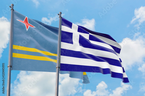 Greece and Aruba flags waving in the wind against white cloudy blue sky together. Diplomacy concept, international relations.