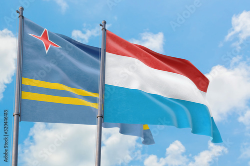 Luxembourg and Aruba flags waving in the wind against white cloudy blue sky together. Diplomacy concept, international relations.