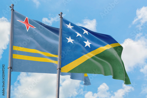 Solomon Islands and Aruba flags waving in the wind against white cloudy blue sky together. Diplomacy concept, international relations.