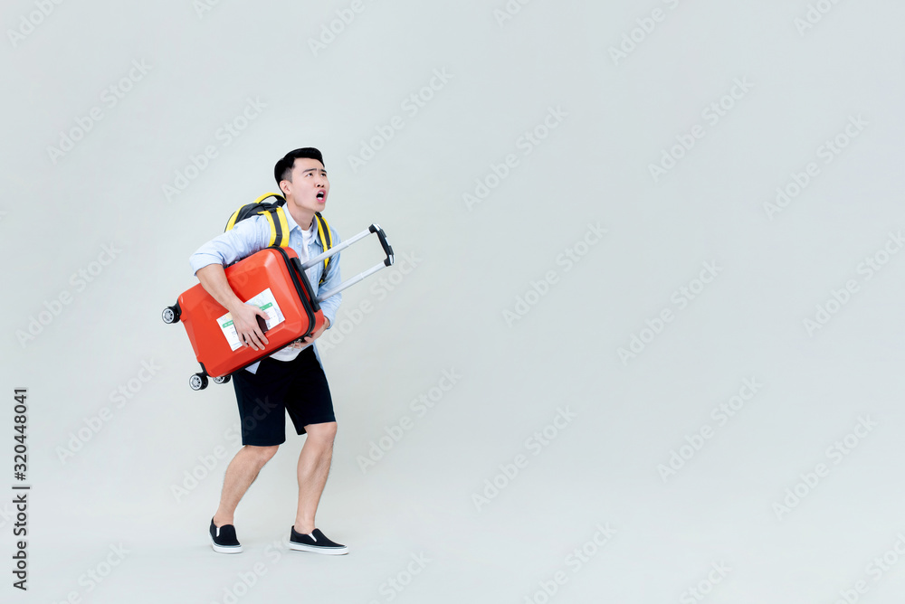 Shocked young Asian man tourist with luggage looking upward Shocked young Asian man tourist with luggage looking upward