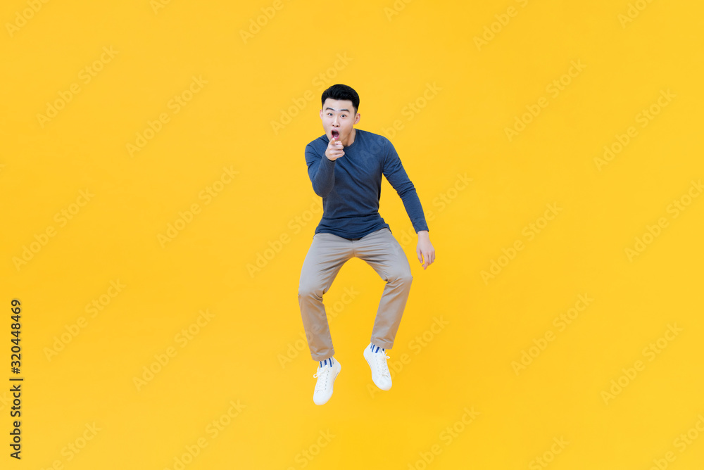 Asian man jumping in mid-air doing pointing gesture