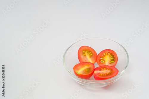 Half of red cherry tomato in glass bowl on white background and copy space