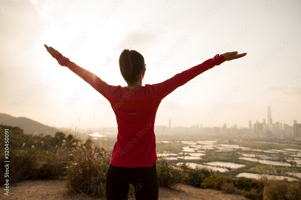 Cheering female open arms on mountains next to modern city Cheering female open arms on mountains next to modern city