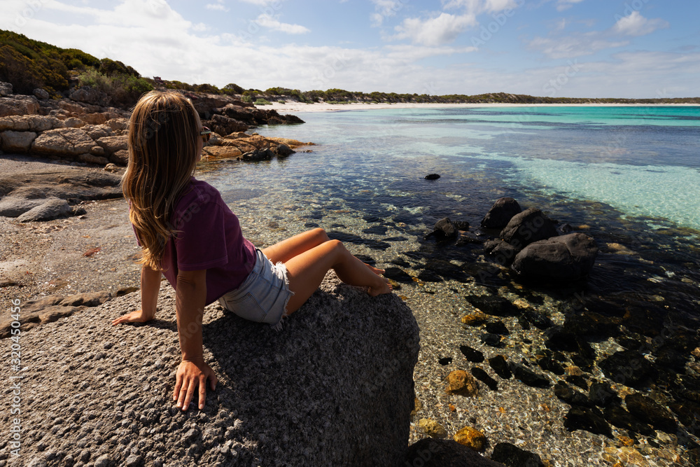 Young woman sitting on a rock by the sea with view of pristine coastline on sunny day in South Australia
