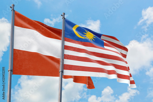Malaysia and Austria flags waving in the wind against white cloudy blue sky together. Diplomacy concept  international relations.