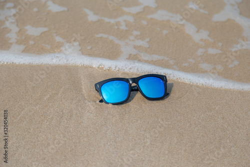 Blue fashion sun glasses on the sand with wave and beach