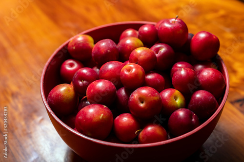 Bowl full of red summer plums on a wooden kitchen bench