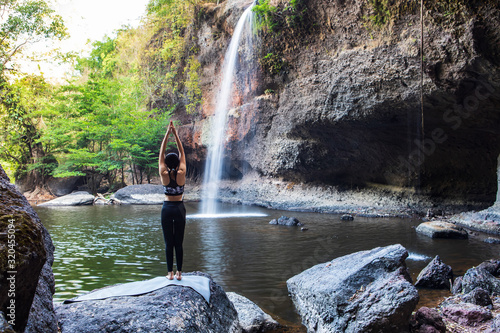 Young girl asian women is playing yoga in front of the waterfall.