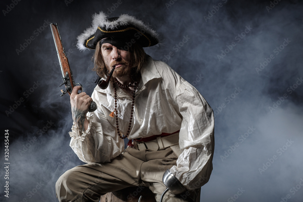 Fototapeta premium średniowieczny pirat brodaty z mieczem i pistoletem. koncepcja zdjęcie przystojny mężczyzna w pirackim kostiumie vintage z pistoletem i szablą
