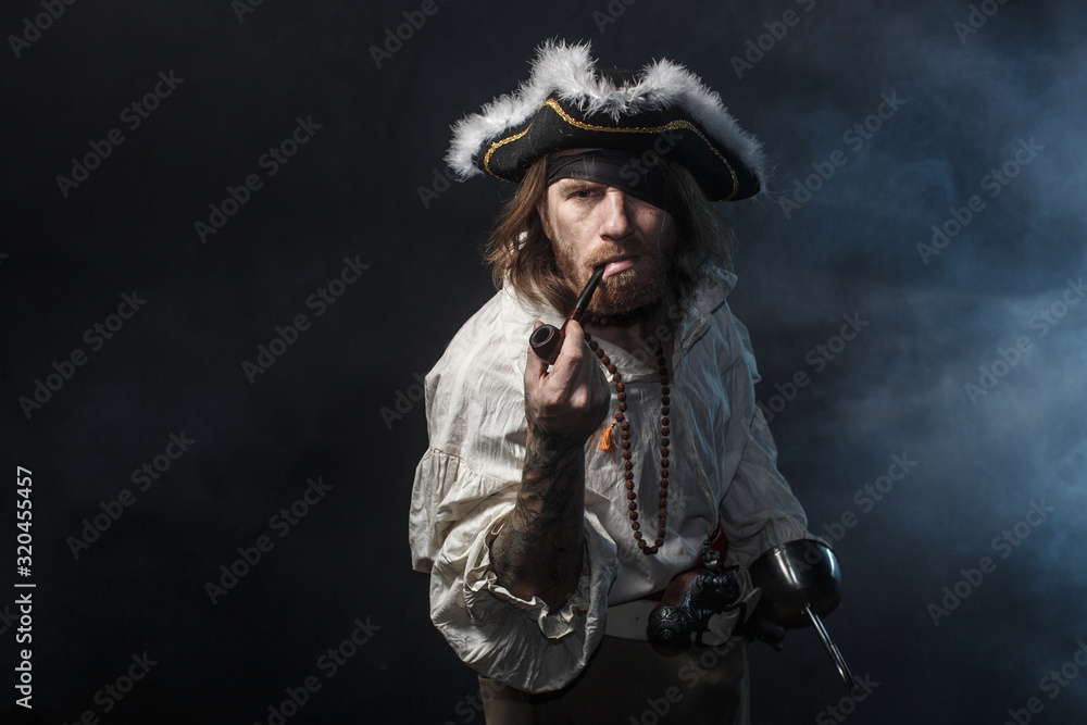 Fototapeta premium średniowieczny pirat brodaty z mieczem i pistoletem. koncepcja zdjęcie przystojnego mężczyzny w pirackim kostiumie vintage z pistoletem i szablą