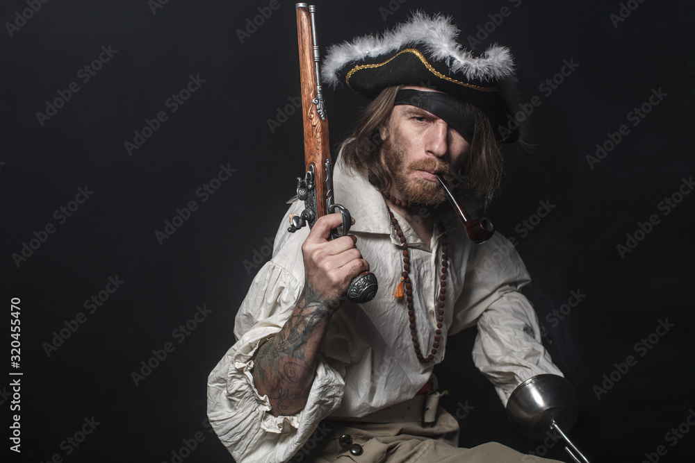 Fototapeta premium średniowieczny pirat brodaty z mieczem i pistoletem. koncepcja zdjęcie przystojnego mężczyzny w pirackim kostiumie vintage z pistoletem i szablą