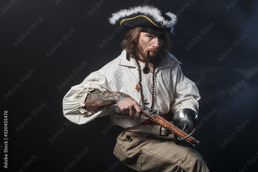 Obraz premium średniowieczny brodaty pirat z mieczem i pistoletem. koncepcja zdjęcie przystojny mężczyzna w pirackim kostiumie vintage z pistoletem i szablą