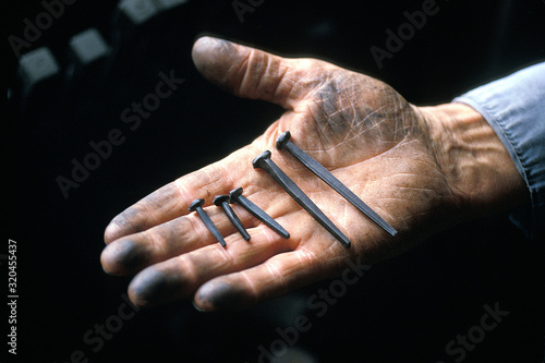 Cropped image of dirty blacksmith hand holding forged nails  photo