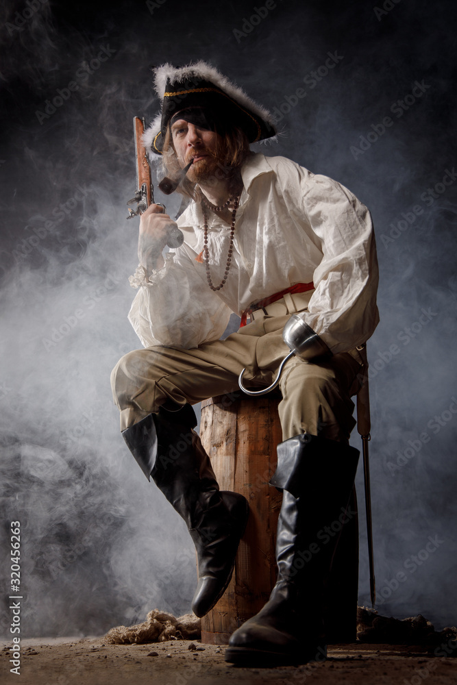 Pirate filibuster sea robber in suit with gun and saber sits on barrel. Concept photo