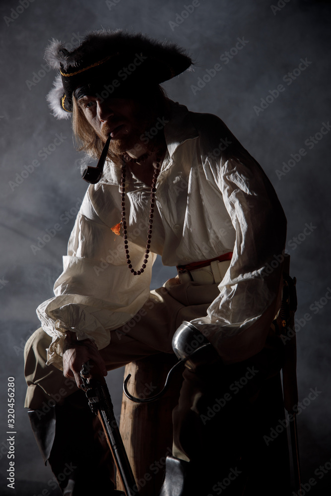 Fototapeta premium Pirate filibuster sea robber in suit with gun and saber sits on barrel. Concept photo