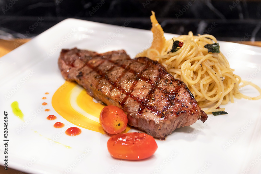 Medium grilled striploin beef steak with spaghetti olio a side dish served on white dish. Medium grilled striploin beef steak with spaghetti olio a side dish served on white dish.