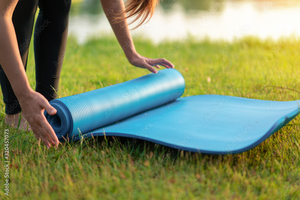 Young asian woman rolling blue yoga mat or fitness mat prepare to exercise in park, Healthy concept, Mind-body improvements concept. - obrazy, fototapety, plakaty 