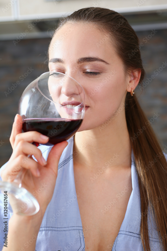 Beautiful smiling brunette woman hold in arms glass of red wine at kitchen table portrait. Vine cabernet merlot sauvignon lips beauty concept Beautiful smiling brunette woman hold in arms glass of red wine at kitchen table portrait. Vine cabernet merlot sauvignon lips beauty concept