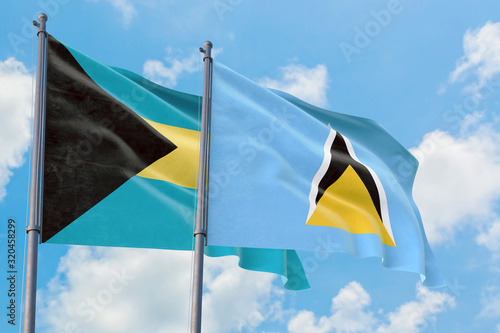 Saint Lucia and Bahamas flags waving in the wind against white cloudy blue sky together. Diplomacy concept, international relations.