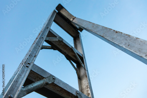 Gardening tool and equipment. A single aluminum garden ladder standing under the clear sky. Close-up and low angle view © Valmedia