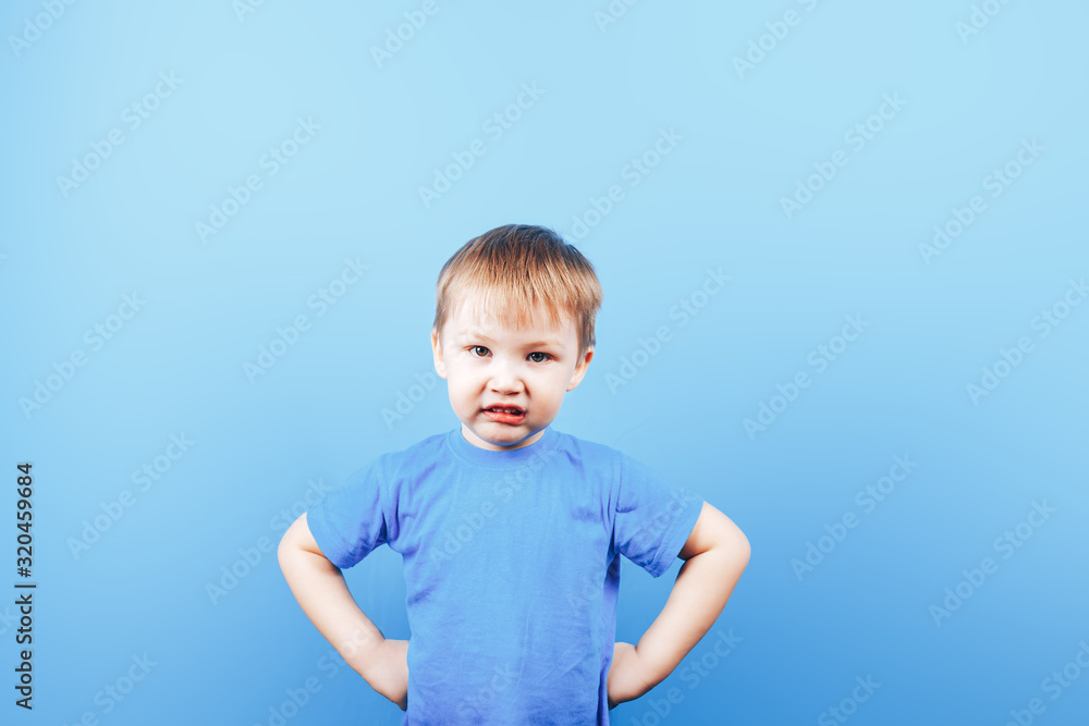 Small angry boy looking at camera on blue background. Small angry boy looking at camera on blue background.