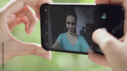 Young pretty woman takes selfie. Closeup hand holding phone.