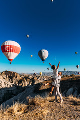 Honeymoon trip. Couple in love among balloons. A man proposes to a girl. Couple in love in Cappadocia. Couple in Turkey.  Man and woman traveling. Festival of balloons. The couple travels the world