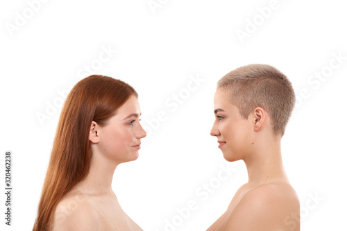 We're all different. Two attractive blonde and red hair women with clean and fresh skin standing opposite each other while posing naked against white background. Natural beauty