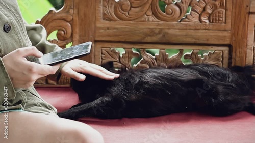 Young woman writes a message on the phone and plays with a black dog