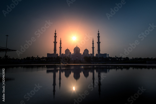 The Sheikh Zayed Grand Mosque with reflection on water and a beautiful golden hour sunset view