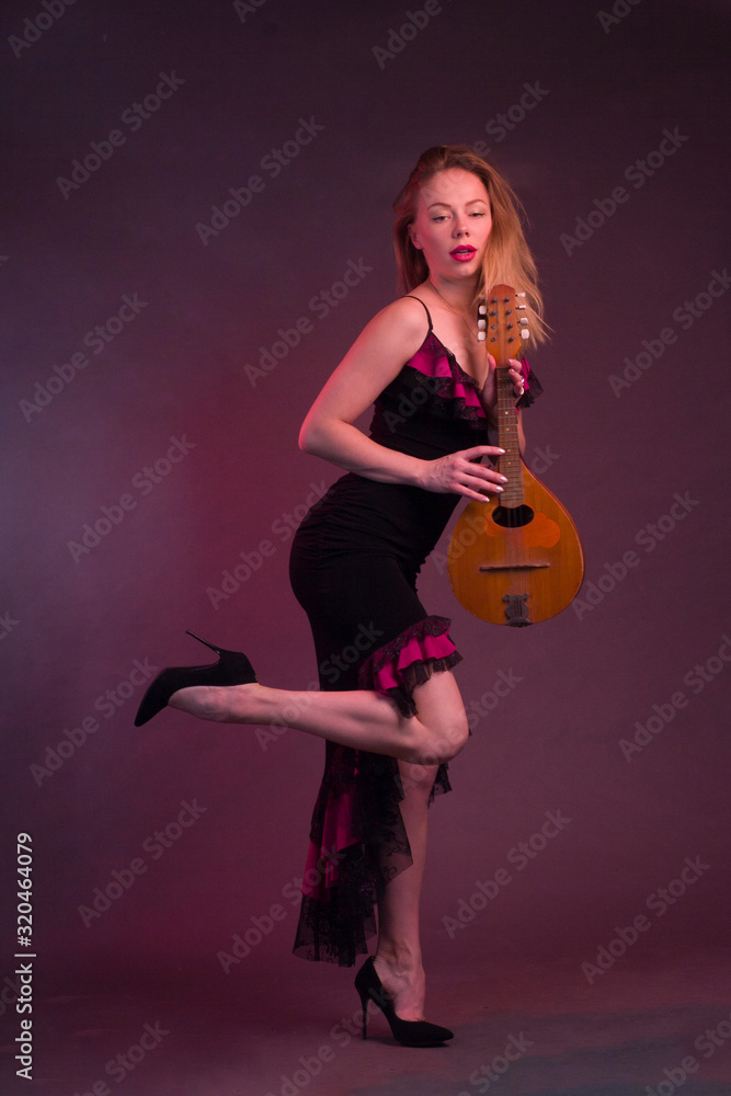 Blonde, in a black Spanish Dressdress flamenco dancer in action, with a mandolin in her hands on a Burgundy background of the Studio Blonde, in a black Spanish Dressdress flamenco dancer in action, with a mandolin in her hands on a Burgundy background of the Studio