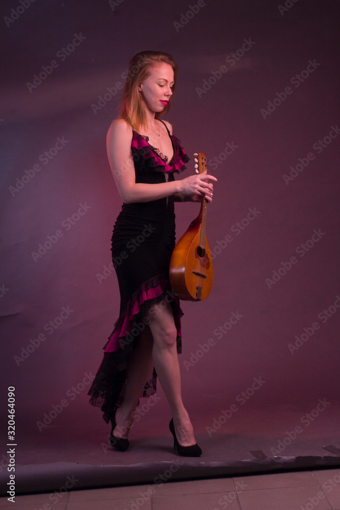 Blonde, in a black Spanish Dressdress flamenco dancer in action, with a mandolin in her hands on a Burgundy background of the Studio Blonde, in a black Spanish Dressdress flamenco dancer in action, with a mandolin in her hands on a Burgundy background of the Studio