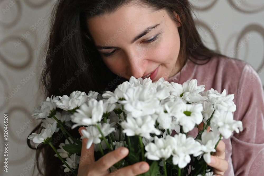 Girl sniffs a bouquet of white flowers. Brunette hugs sniffs a bouquet of delicate flowers from her beloved. A nice gift for your beloved half. Girl sniffs a bouquet of white flowers. Brunette hugs sniffs a bouquet of delicate flowers from her beloved. A nice gift for your beloved half.